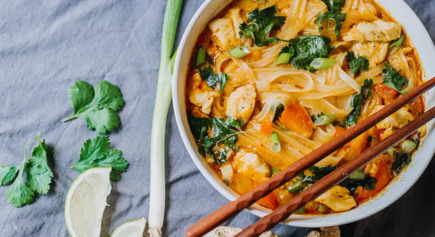 Miseczka z tajską zupą curry z kurczakiem, makaronem ryżowym i warzywami, podana z pałeczkami.
