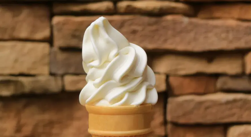 Ein cremiges Vanilleeis mit Ei im Waffelhörnchen, vor einer rustikalen Steinwand.