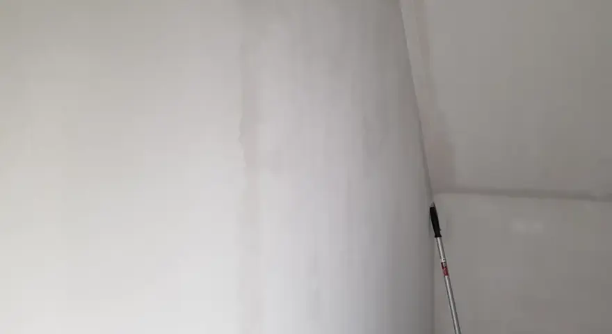 En lång skrapa med handtag står lutad mot en nyspacklad vägg, redo att slipa spackel för en slät yta.
