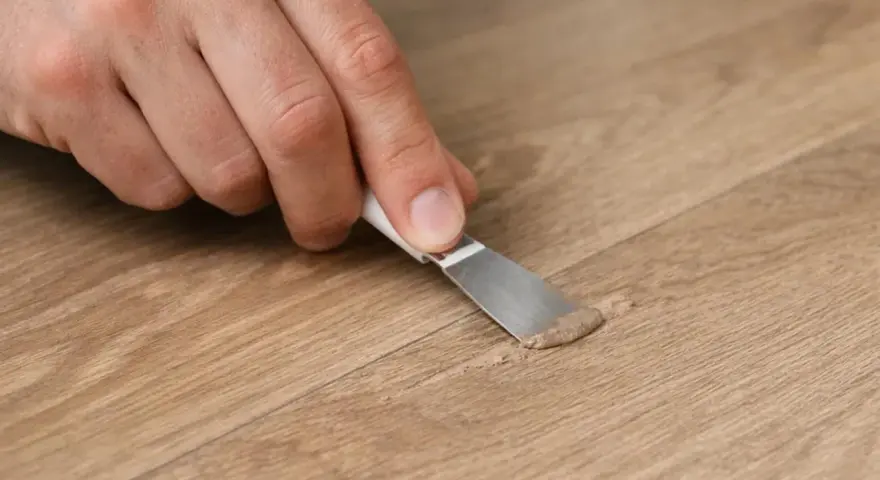 Mano che ripara un piccolo buco nel muro con una spatola e stucco.