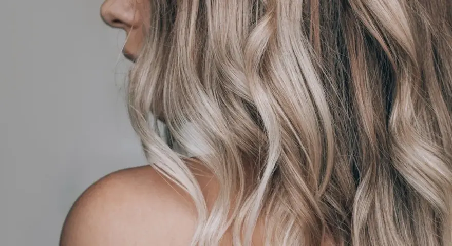 Kobieta z falowanymi, blond włosami ozdobionymi nowoczesnymi pasemkami, ukazana od ramienia.