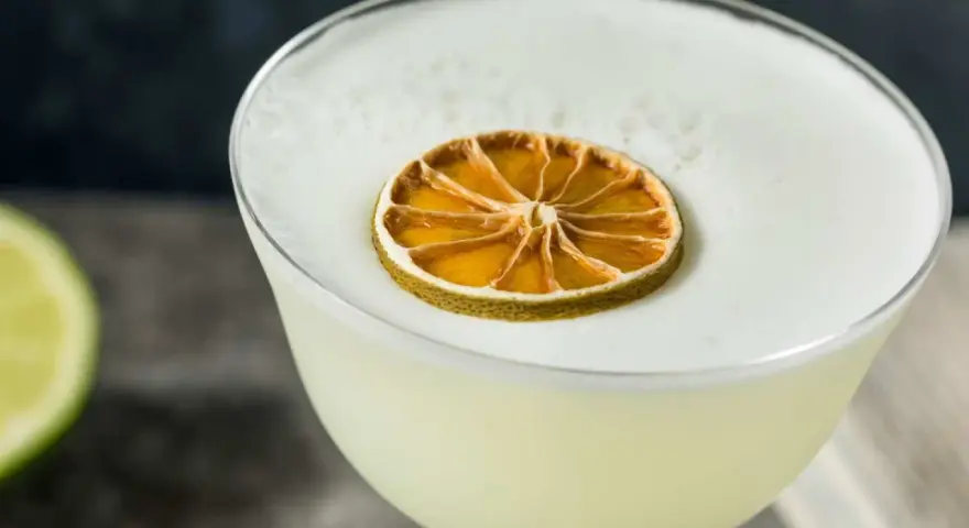 En krämig gin sour med ett skumtäcke och en torkad lime som dekoration.