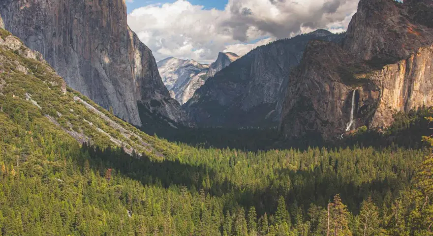 Majestatyczne klify i wodospad w **parku narodowym Yosemite**, otoczone gęstym lasem iglastym.