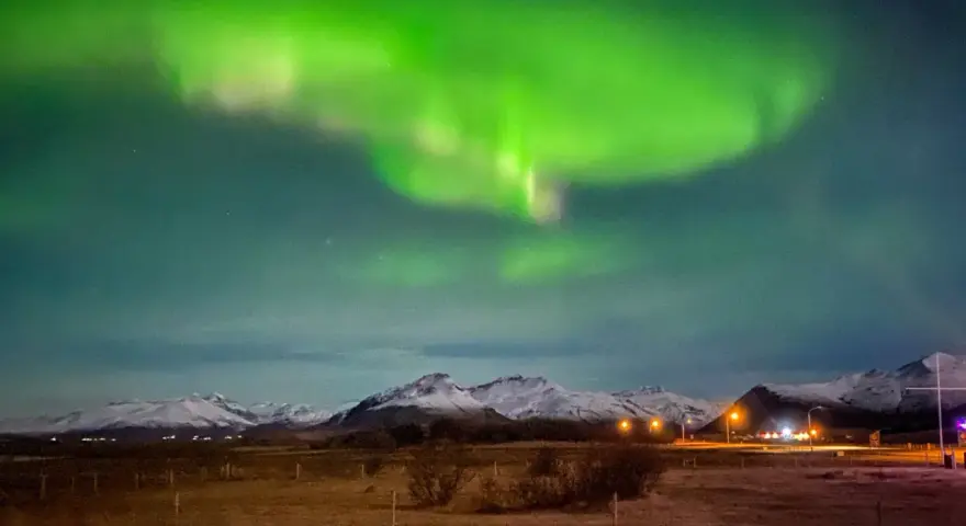 Islandia pogoda luty: zielona zorza polarna nad ośnieżonymi górami i polami.
