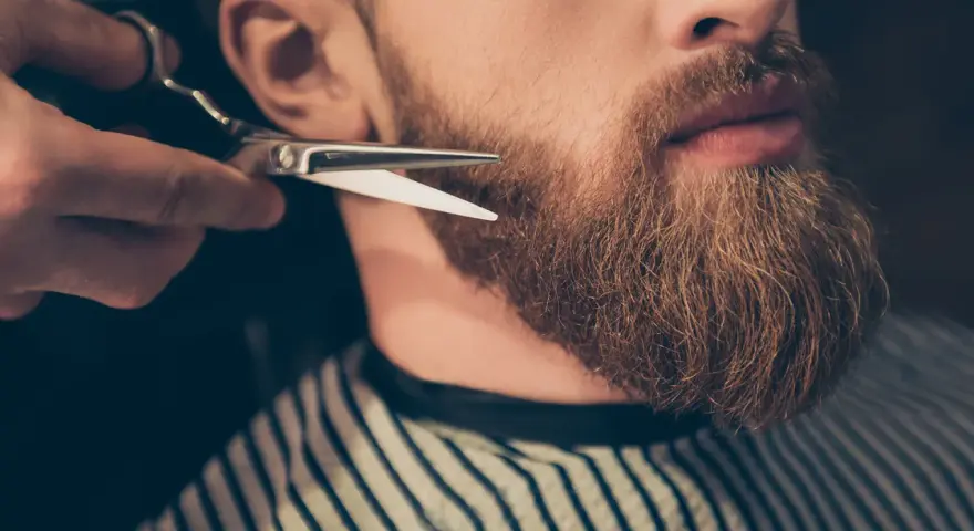 Un barbero recorta una barba larga y rojiza con tijeras.