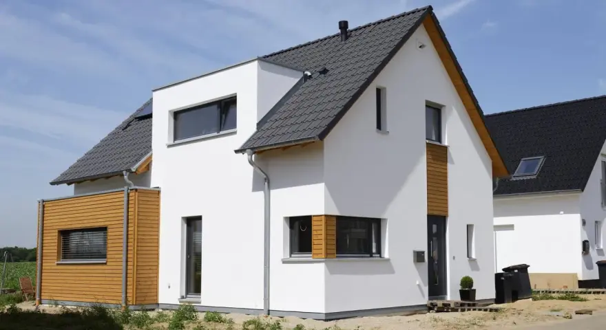 Moderner Neubau trocknet im Sonnenschein. Weiße Fassade, Holzverkleidung und dunkles Dach.