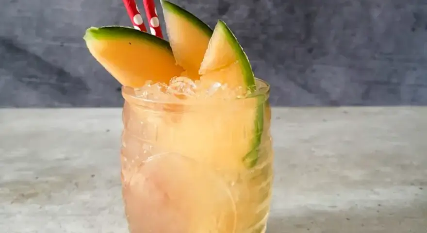 Orzeźwiający drink z mango, ozdobiony plasterkami owocu i dwoma czerwono-białymi słomkami. Idealny na upalne dni.
