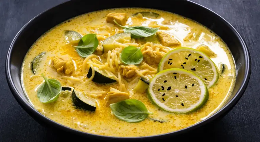 Aksamitne curry z kurczakiem, makaronem i plasterkami cukinii, ozdobione świeżą bazylią i limonką.