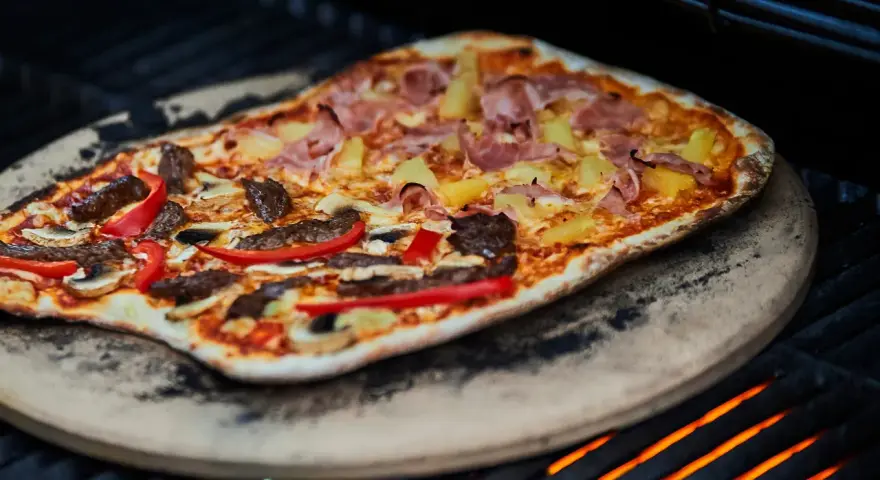 En läcker pizza på grillen med skinka, ananas, kött och paprika. En perfekt sommarmåltid!