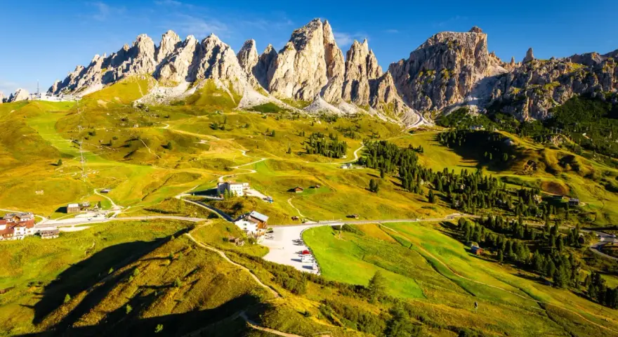 Panorami mozzafiato sull'**Alta Via numero 2 Dolomiti**. Sentieri serpeggianti tra prati verdi e imponenti vette rocciose sotto un cielo azzurro.