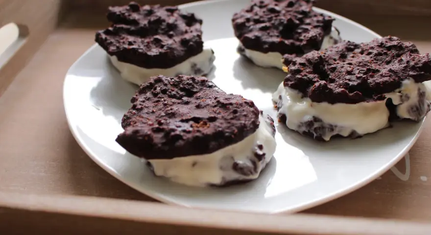 Cztery domowe ciastka z kremem, przypominające Oreo, na białym talerzu. Pyszna przekąska, choć warto sprawdzić oreo kcal przed zjedzeniem.