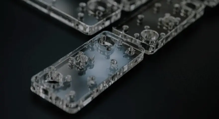 Rows of clear acrylic phone cases, showcasing their intricate internal designs and precise cuts, are laid out on a dark surface.