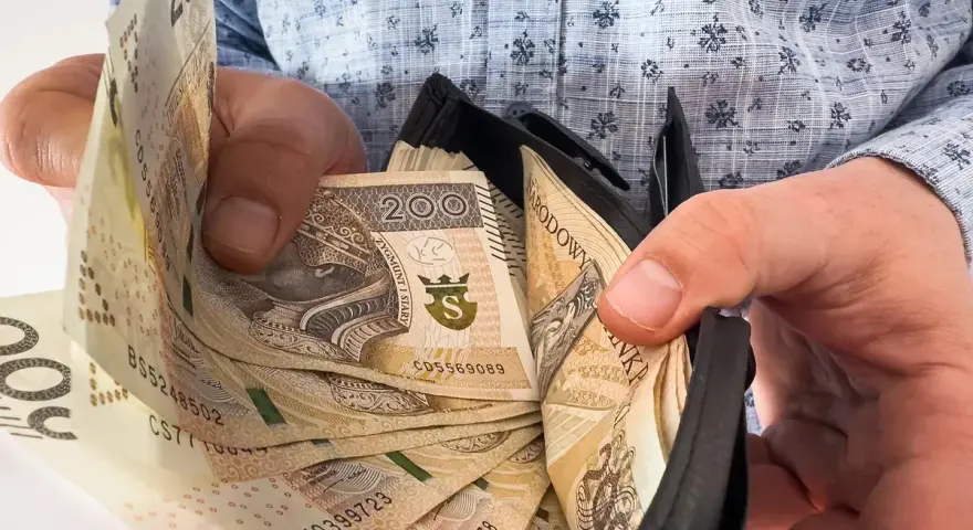 Ręce trzymają portfel z banknotami 200 zł. To symboliczne przedstawienie nagrody jubileuszowej za 15 lat pracy.