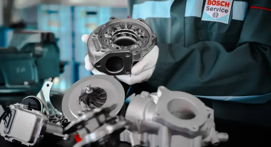 Mechanik w kombinezonie Bosch Service prezentuje części turbosprężarki, kluczowe dla eliminacji turbo lag.