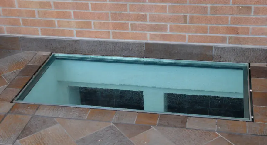 Bocche di lupo moderne in vetro, incastonate in un pavimento di piastrelle color terra, illuminano uno spazio sottostante.