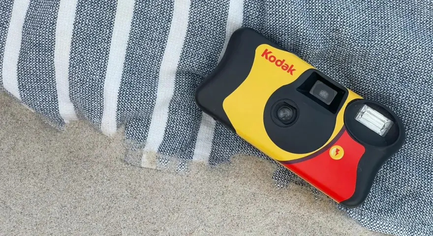 Aparat jednorazowy firmy Kodak leży na plaży obok ręcznika. Idealny do uchwycenia letnich wspomnień.