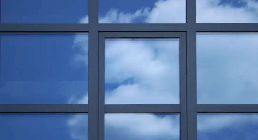 Szpros dzieli okno na kwadratowe pola, w których odbija się błękitne niebo z chmurami.