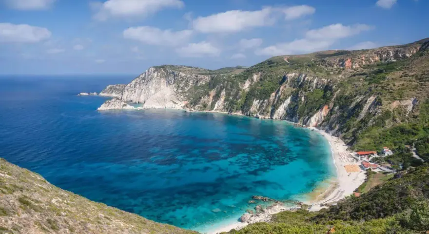 Malownicza zatoka z turkusową wodą i piaszczystą plażą, otoczona stromymi, zielonymi klifami. To idealne miejsce na wypoczynek na wyspie na Morzu Jońskim.