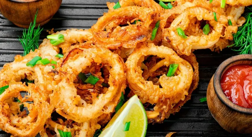 Aros de calamar rebozados y fritos, servidos con limón y salsa de tomate. Ideales para recetas con calamares.