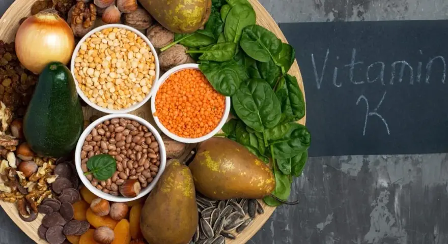 En bricka med mat rik på vitamin K1: spenat, päron, avokado, nötter, linser, bönor, torkade aprikoser, solrosfrön och choklad.