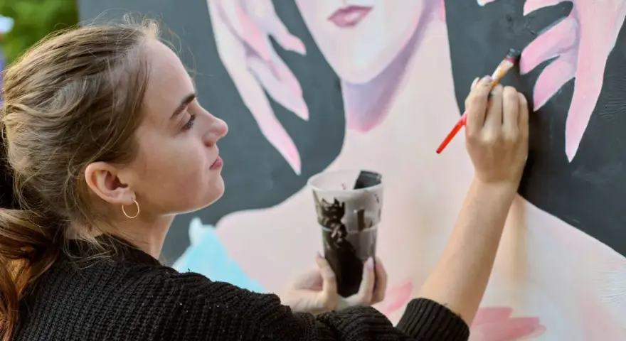 Une jeune artiste entrepreneur peint un portrait. Elle tient un pinceau et un gobelet de peinture noire.