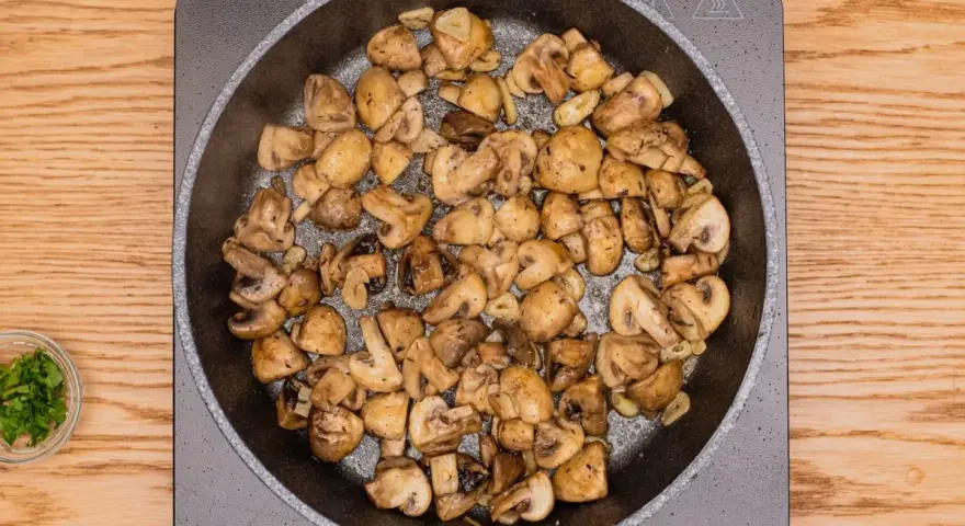 Champiñones al ajillo dorándose en sartén, con ajo y perejil picado al lado.