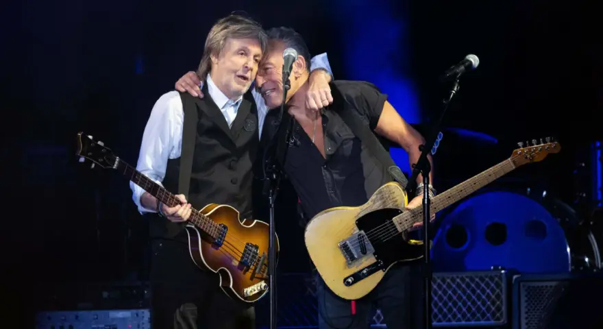 Bruce Springsteen und Paul McCartney umarmen sich auf der Bühne, beide mit Gitarren.