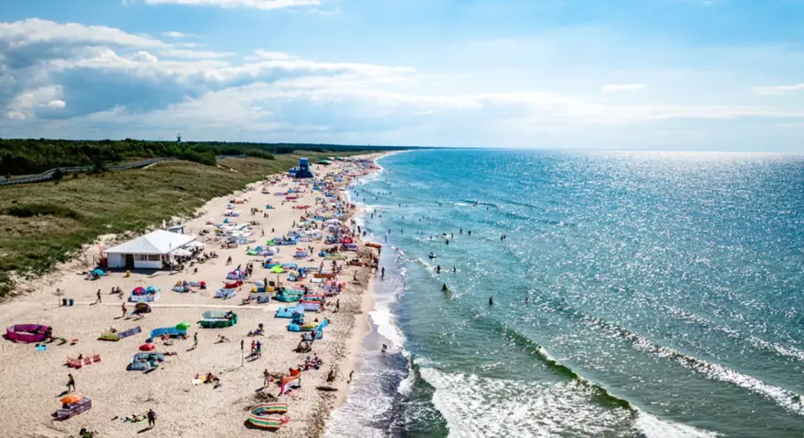 Słoneczna plaża w Darłówku pełna ludzi, kolorowych parawanów i namiotów. Woda w Bałtyku błyszczy, a fale zachęcają do kąpieli. To idealne miejsce na wakacyjne atrakcje.