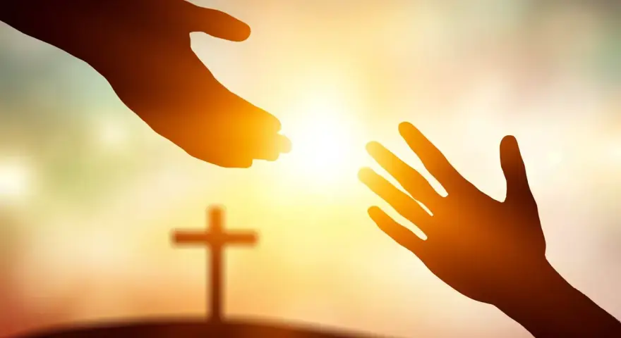Zwei Hände reichen sich im warmen Licht entgegen, ein Kreuz im Hintergrund symbolisiert die Hilfe von Jesus Christus.