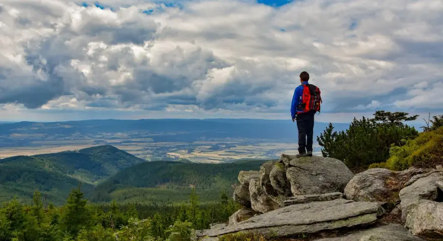 Turysta z plecakiem podziwia rozległą panoramę Gór Opawskich. Chmury na niebie tworzą dramatyczny spektakl.