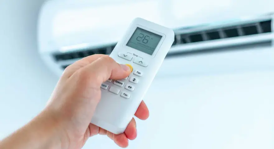 Dłoń trzymająca pilot do klimatyzatora, ustawiająca temperaturę. Ogrzewanie klimatyzatorem to komfort.
