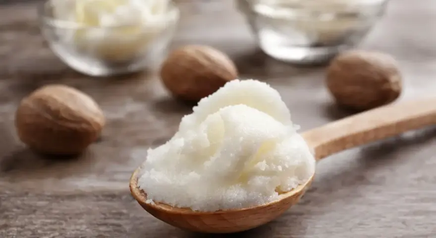 Ein Holzlöffel voller cremiger shea butter haare, daneben Nüsse und Schalen mit der Butter.