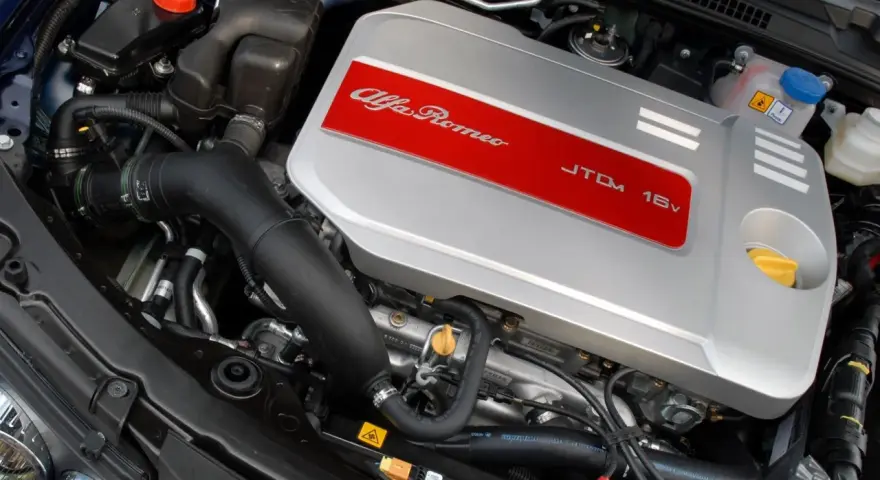Silnik Alfa Romeo 1.9 JTD 16V z widocznym srebrnym deklom z czerwonym pasem i napisem.