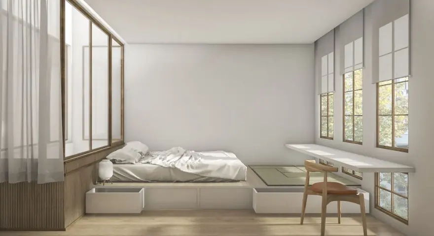 Camera da letto minimalista con letto feng shui, tatami, scrivania a muro e grandi finestre con vista su alberi.