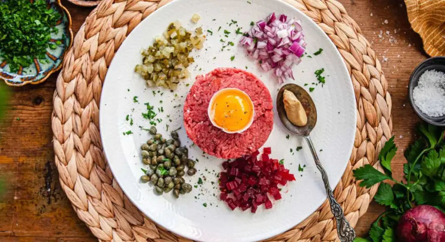 En tallrik med råbiff, äggula, kapris, hackad rödlök, gurka och rödbetor. Perfekt för ett klassiskt råbiff recept.