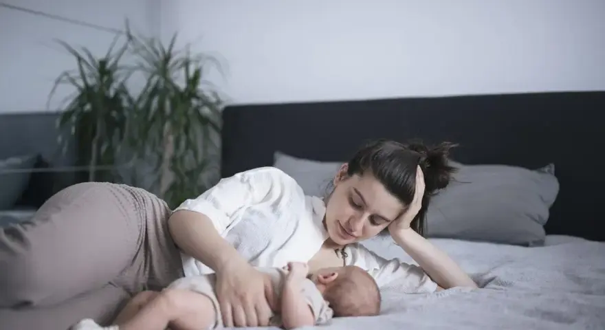 Matka karmi piersią dziecko na leżąco, opierając głowę na dłoni. Czuły moment bliskości.