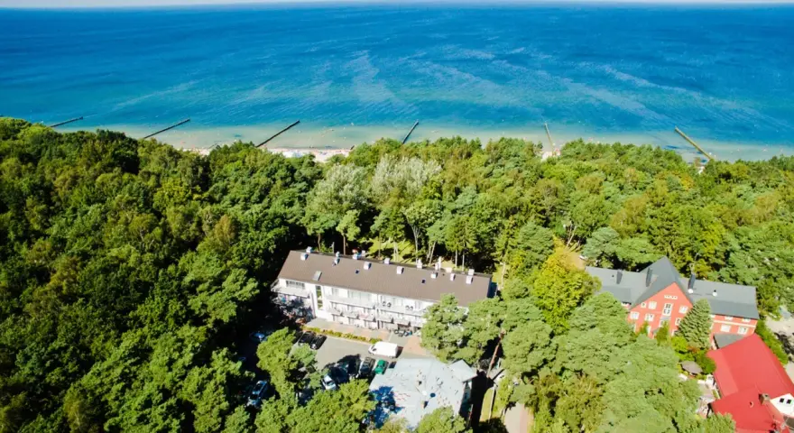 Widok z lotu ptaka na hotel otoczony lasem, z widokiem na morze. Idealne miejsce na wakacje, sprawdź nasz tui kod rabatowy!