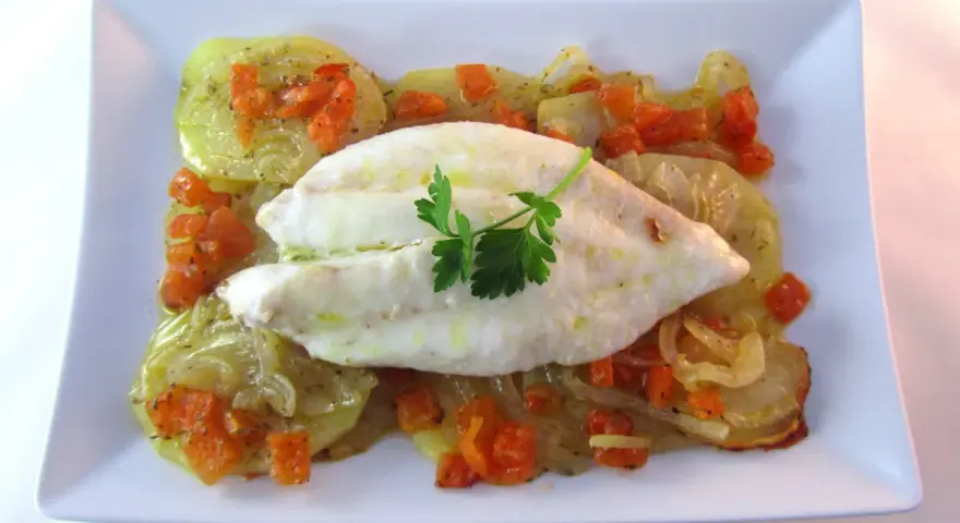 Filete de pescado blanco sobre patatas y zanahorias asadas, un delicioso gallo al horno.