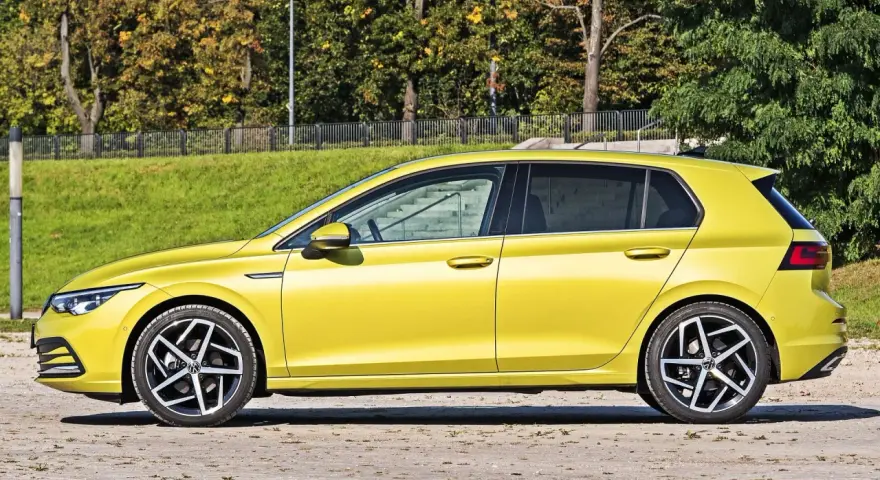 Żółty hatchback Volkswagen Golf VIII z przyciemnianymi szybami stoi na tle zieleni i drzew.