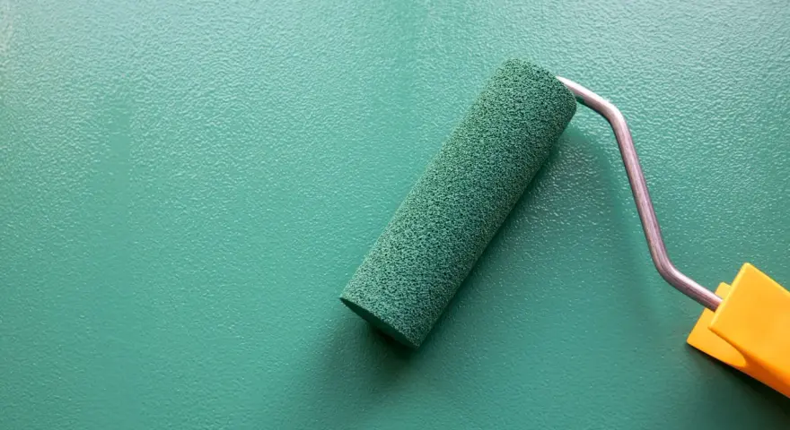 Rodillo de pintura verde sobre pared texturizada. Se puede pintar sobre papel pintado para renovar espacios.