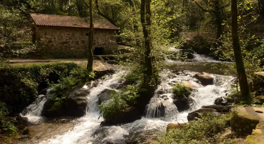 Antigua casa de piedra junto a un río con cascadas, ideal para una ruta senderismo Vigo.