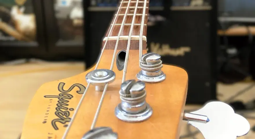 Nahaufnahme des Bass-Kopfes mit Saiten und Stimmmechaniken. Der Schriftzug "Squier by Fender Jazz Bass" ist sichtbar. Perfekt, um den Bass einzustellen.