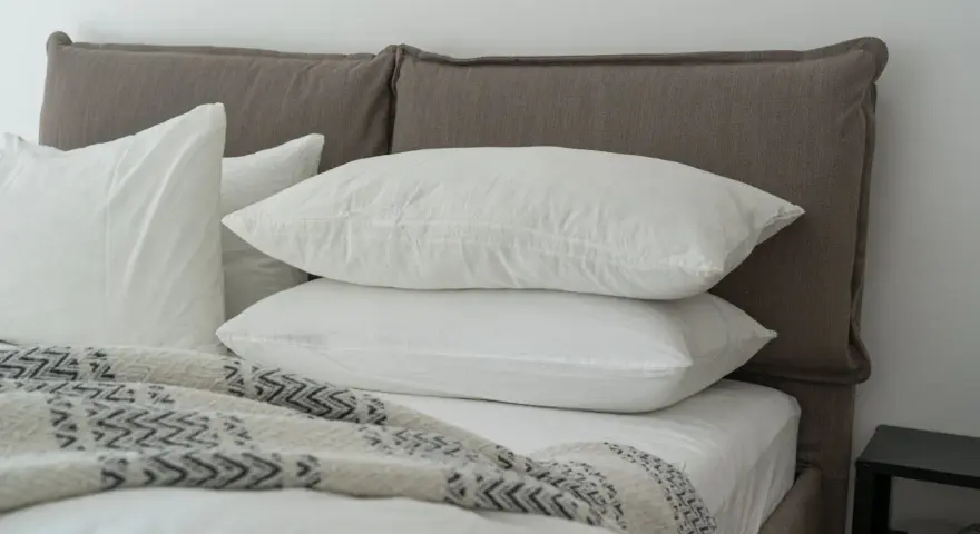 Lit douillet avec deux oreillers blancs empilés, une couverture à motifs et un drap housse ou protège matelas immaculé.
