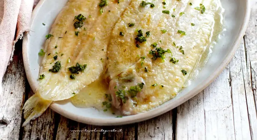 Sogliola alla mugnaia dorata e succulenta, cosparsa di prezzemolo fresco, servita su un piatto ovale.