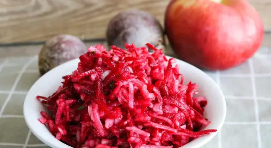Frischer Salat aus rote Bete raspeln, mit einem Apfel und ganzen Rote Beten im Hintergrund.
