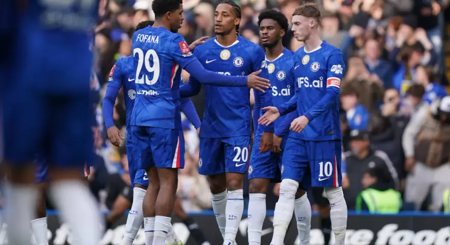 Piłkarze Chelsea w niebieskich strojach rozmawiają na boisku. Widać numery 29, 20 i 10.