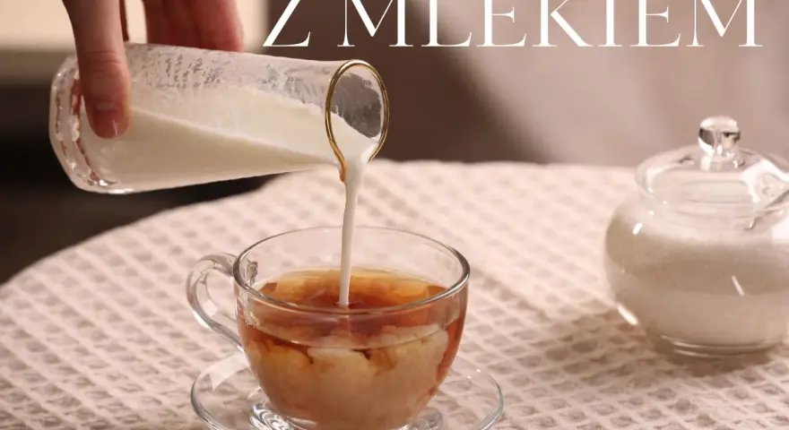 Ręka wlewa mleko do szklanki z herbatą, tworząc piękne smugi. Obok stoi cukiernica. Idealna herbata z mlekiem na chłodny dzień.