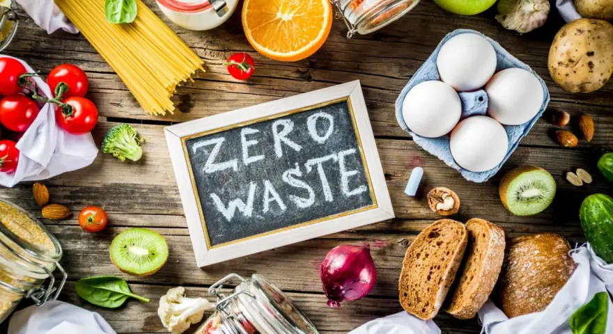 Tablica z napisem "ZERO WASTE" otoczona świeżymi warzywami, owocami, jajkami i produktami sypkimi. Styl życia bez marnowania.