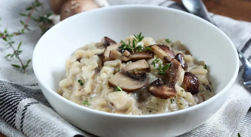 Kremowe risotto z pieczarkami i serem pleśniowym, udekorowane świeżym tymiankiem.