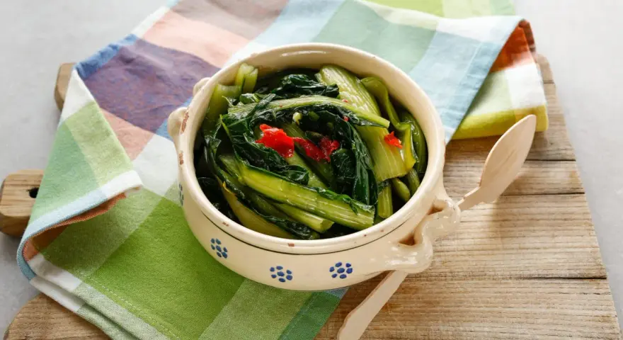 Cicoria in padella, un contorno saporito con peperoncino, servita in una ciotola decorata su un tagliere di legno.